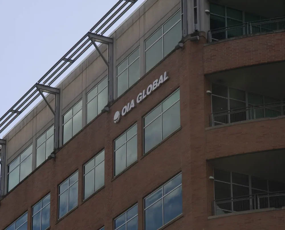 Exterior view of OIA Global headquarters building with large glass windows and company logo displayed on the upper brick facade under a clear sky.