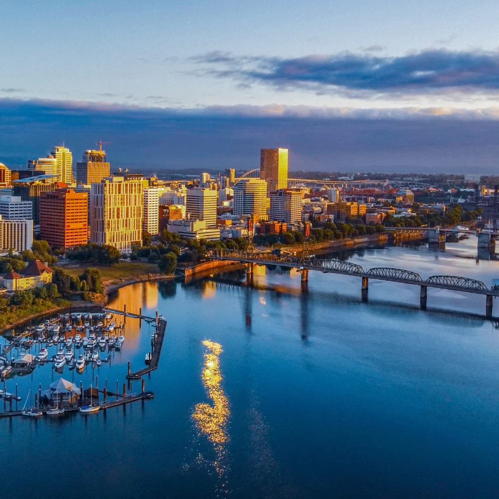 Aerial view of downtown Portland, Oregon at sunrise with high-rise buildings, Willamette River, bridges, and waterfront marina.