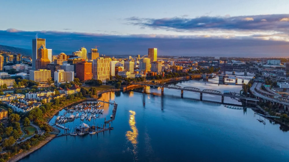 Aerial view of downtown Portland, Oregon at sunrise with high-rise buildings, Willamette River, bridges, and waterfront marina.