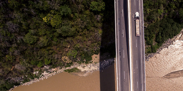 Truck driving across bridge over waterway and forest.