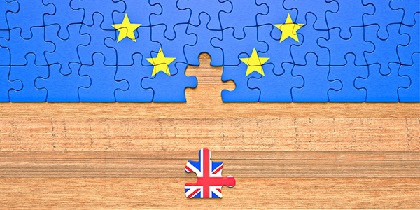 Puzzle representing Brexit with a missing piece in the EU flag and a separate piece featuring the UK flag on a wooden surface.