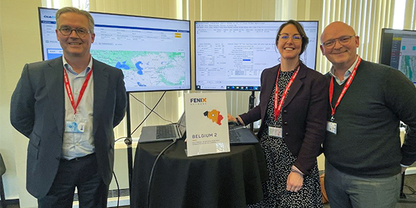 Three professionals standing next to monitors displaying logistics system dashboards and maps during FENIX Project demonstration in Belgium.