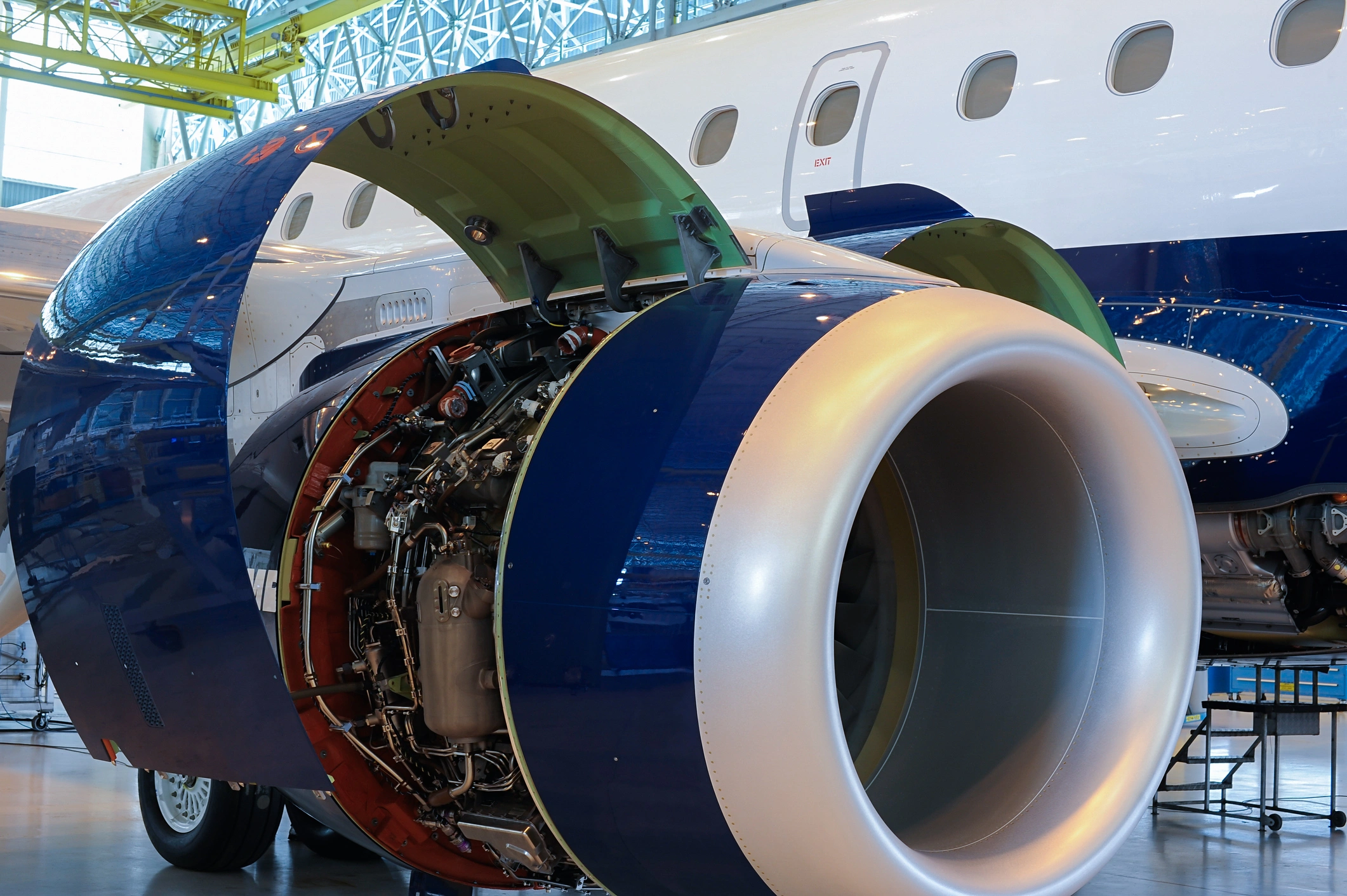 Aircraft engine with open nacelle undergoing inspection and maintenance inside an aviation hangar.