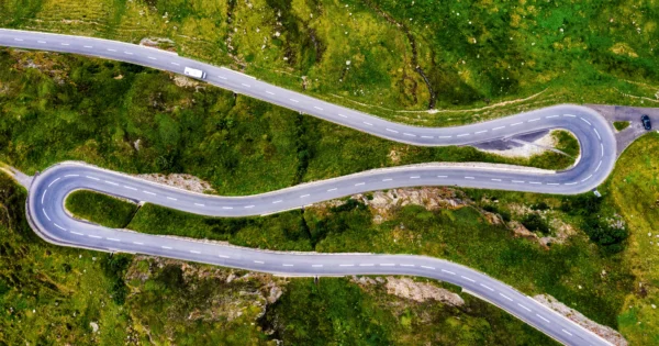 Aerial view of winding mountain road with sharp curves through green landscape and vehicles navigating the route.