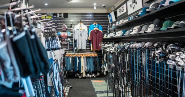 Interior of a golf retail store with racks of golf clubs, apparel, and branded caps displayed on shelves.