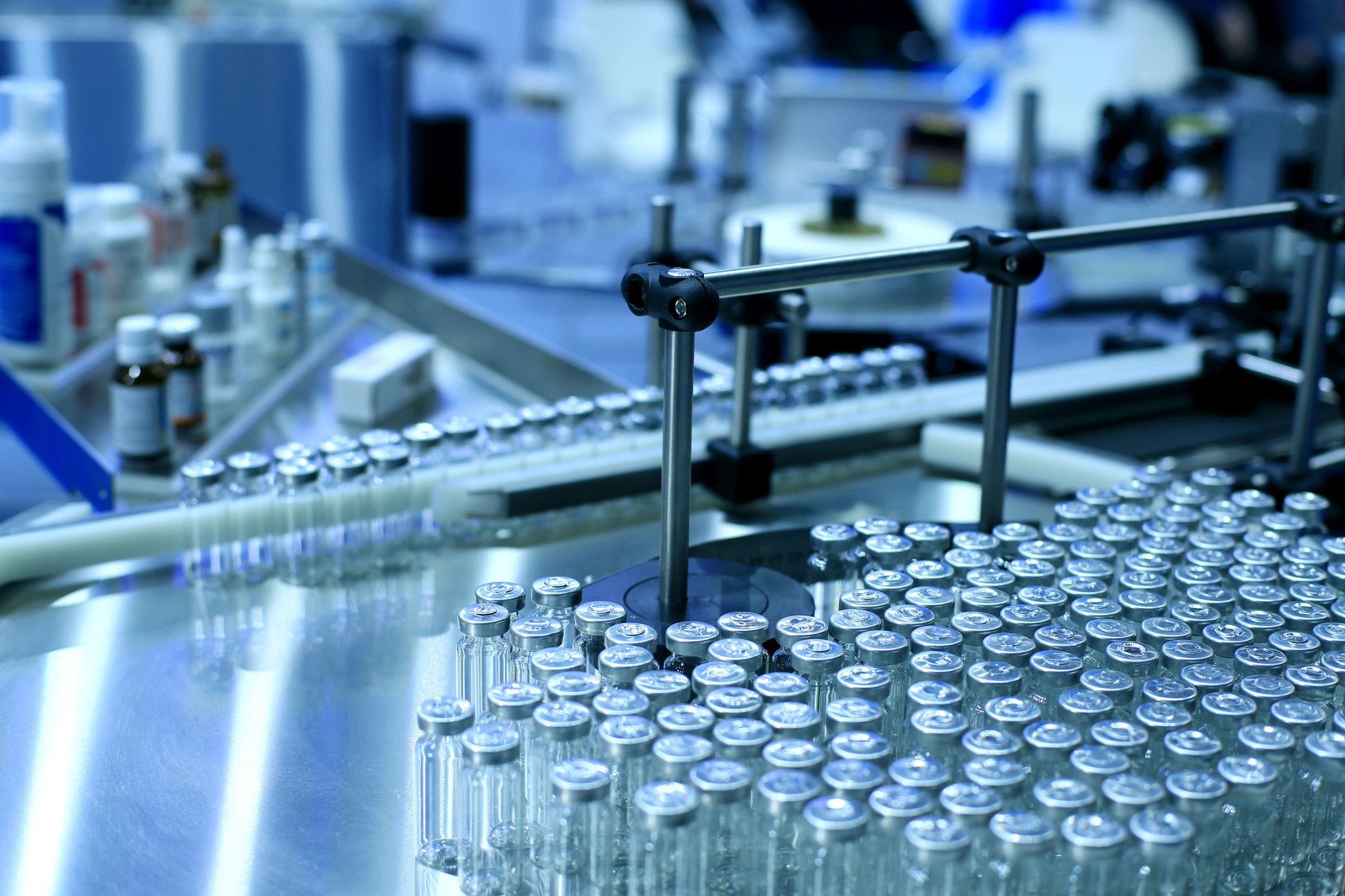 Automated pharmaceutical production line with glass vials on conveyor system in sterile manufacturing environment.