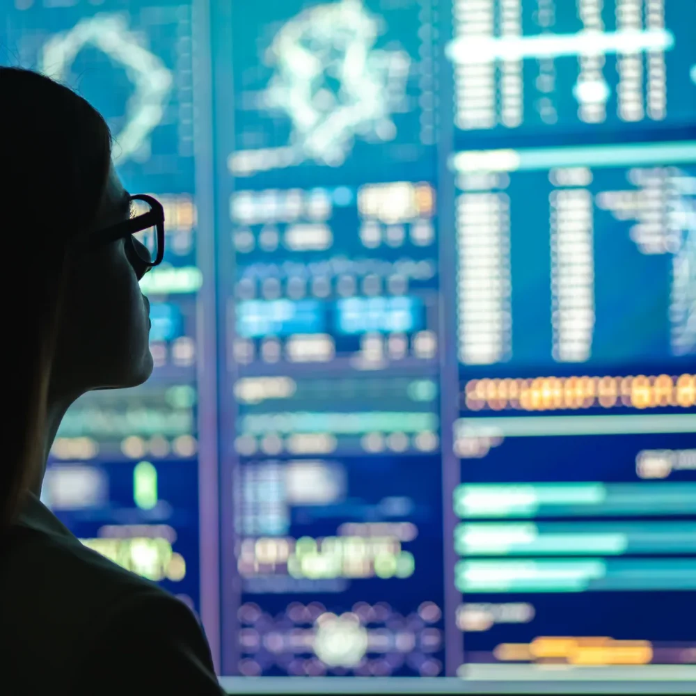 Person analyzing multiple interactive data dashboards on large digital screens displaying charts, graphs, and performance metrics.