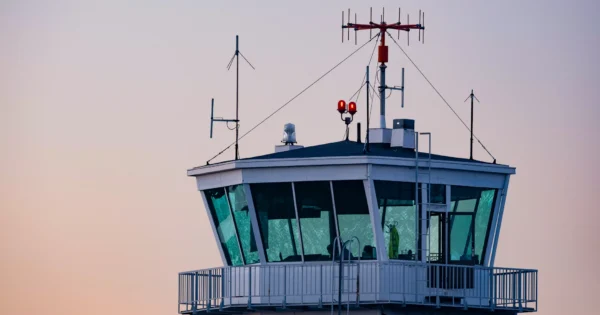 パステルカラーの夕焼け空の下、アンテナや通信機器が並ぶ空港管制塔。