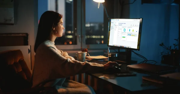 Person working on a desktop computer at night, analyzing data and charts on a business dashboard in a dimly lit home office.