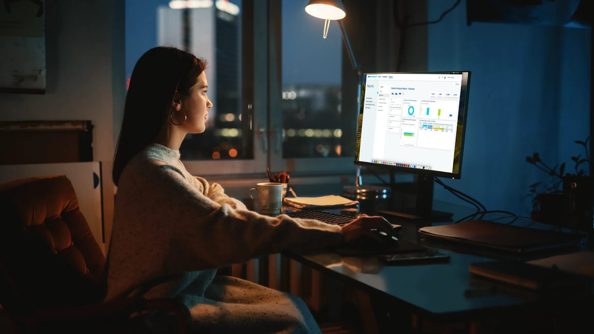 Person working on a desktop computer at night, analyzing data and charts on a business dashboard in a dimly lit home office.