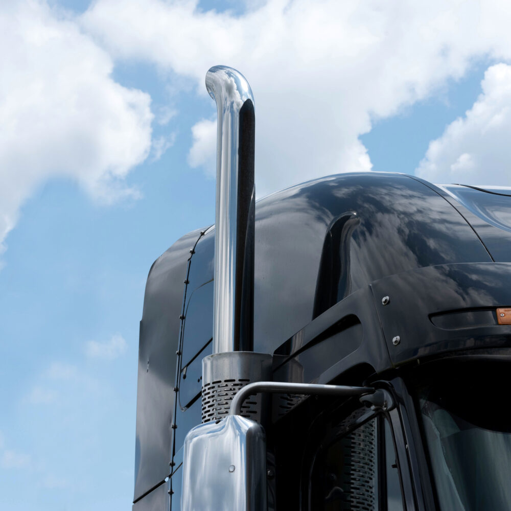 Black semi truck for road freight transportation in front of bright blue sky with clouds representing carbon reporting.