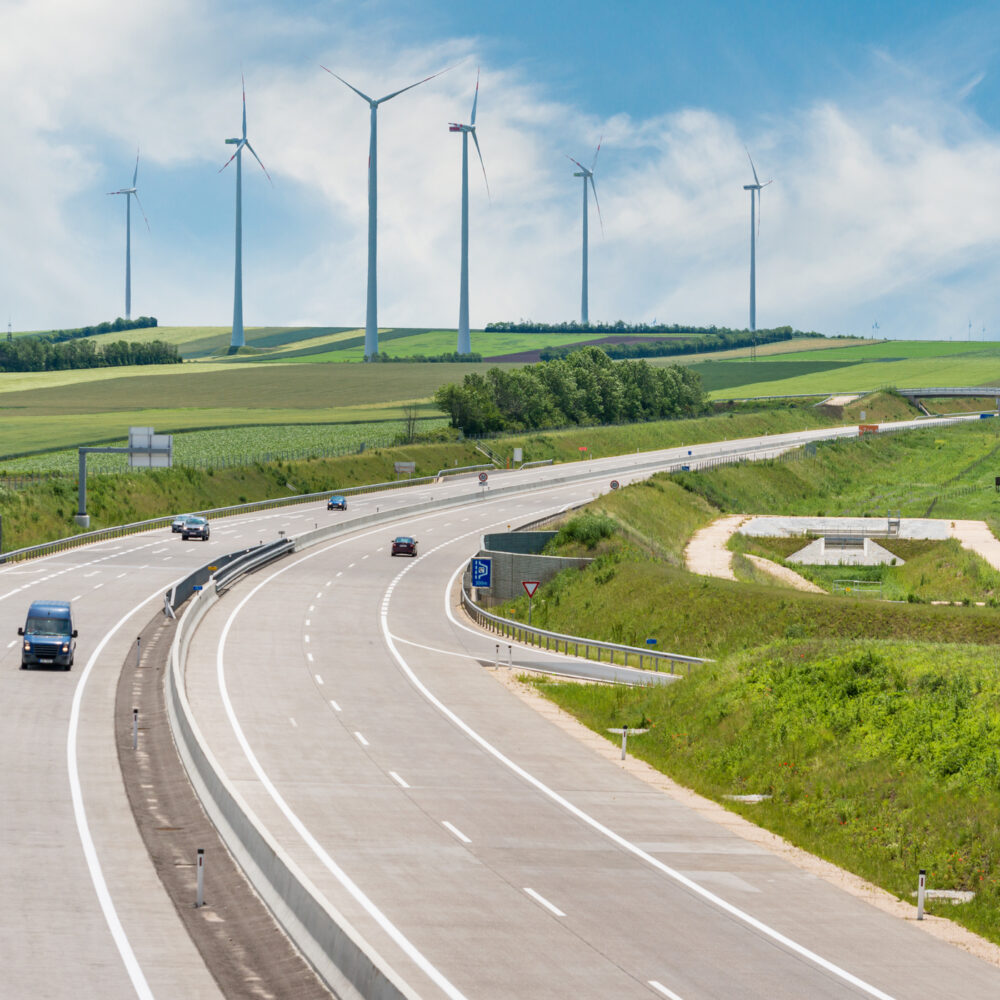 高速公路上的汽车，前方是装有空气涡轮机的绿色田野。