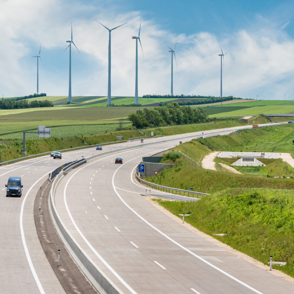 Cars on highway in front of green fields with air turbines.