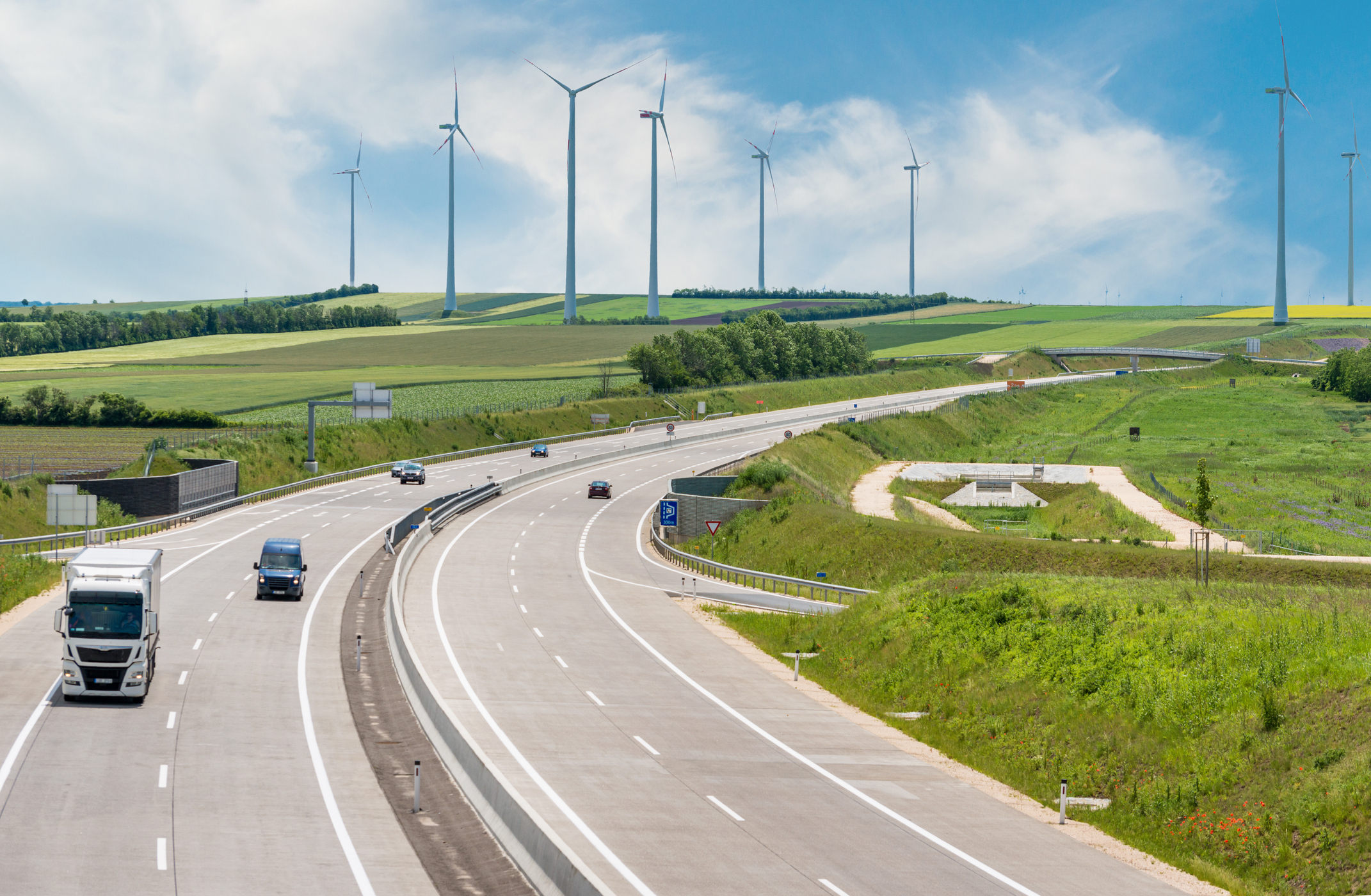 Cars on highway in front of green fields with air turbines.