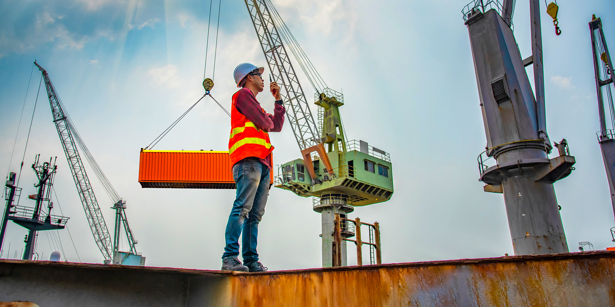 動くクレーンの前で構造物の上に立つ港湾労働者