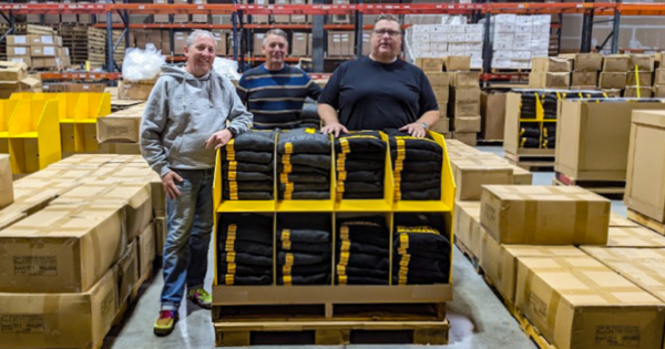 Team members standing behind a palletized display of DeWalt hoodies inside a warehouse filled with boxes and inventory.
