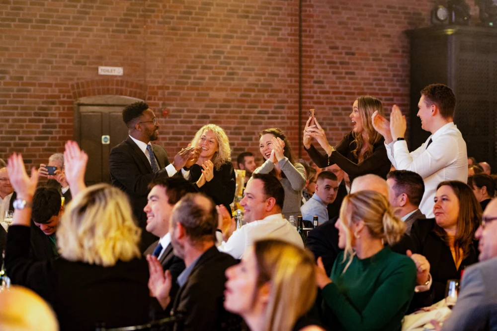 Audience standing and applauding during a corporate awards event in a banquet hall setting.