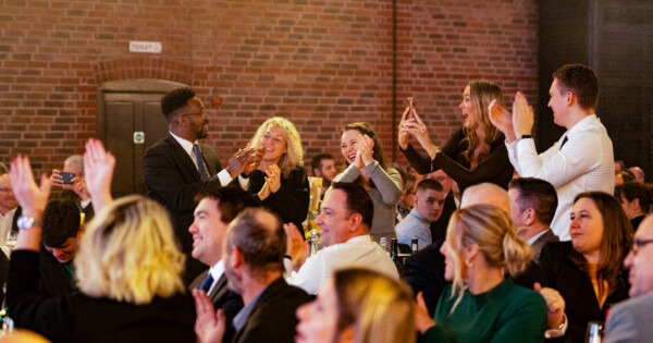 Audience standing and applauding during a corporate awards event in a banquet hall setting.