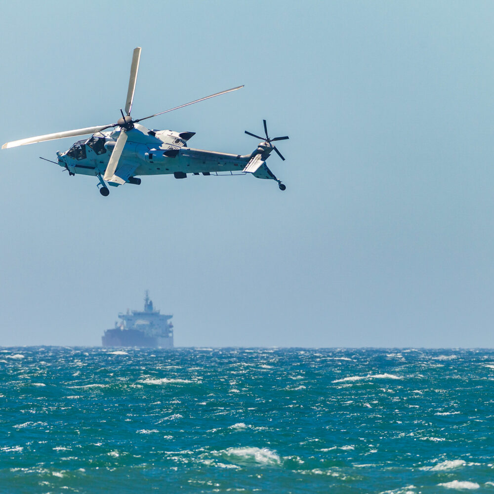 Helicóptero de ataque militar e navio de contêineres no oceano