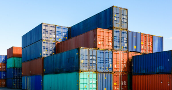 Stacked multicolored shipping containers at a port terminal under a clear blue sky.