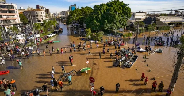 Flooded city street with people wading through water, rescue boats, and submerged vehicles after severe flooding in an urban area.