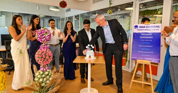 Team celebrating OIA Global shared service center opening in Pune with cake cutting and event signage.