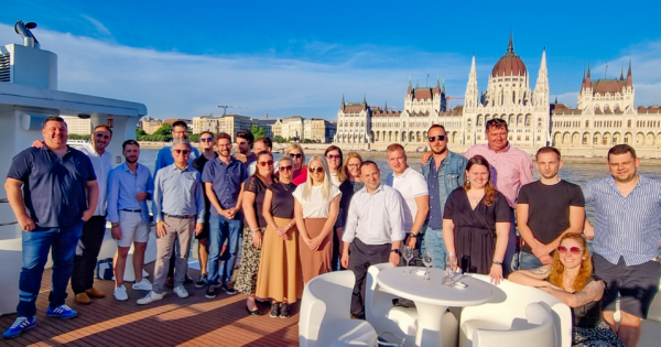 OIA Global Hungary team group photo on a river cruise boat with the Hungarian Parliament building in Budapest in the background.