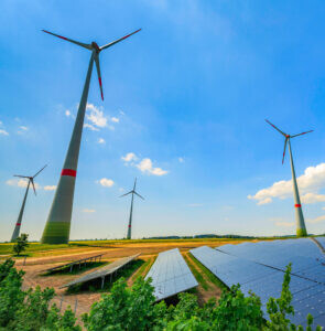 Wind turbines and solar panels in a renewable energy field under a clear blue sky.