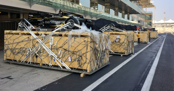 Formula race cars secured in wooden crates with netting at a racetrack, prepared for transport and logistics handling.