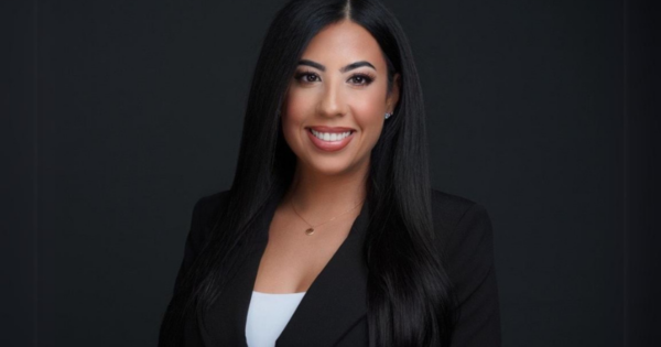 Professional corporate headshot of a business leader in a black blazer against a dark background.