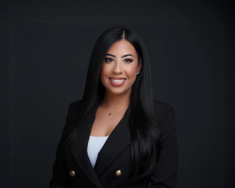 Professional corporate headshot of a business leader in a black blazer against a dark background.