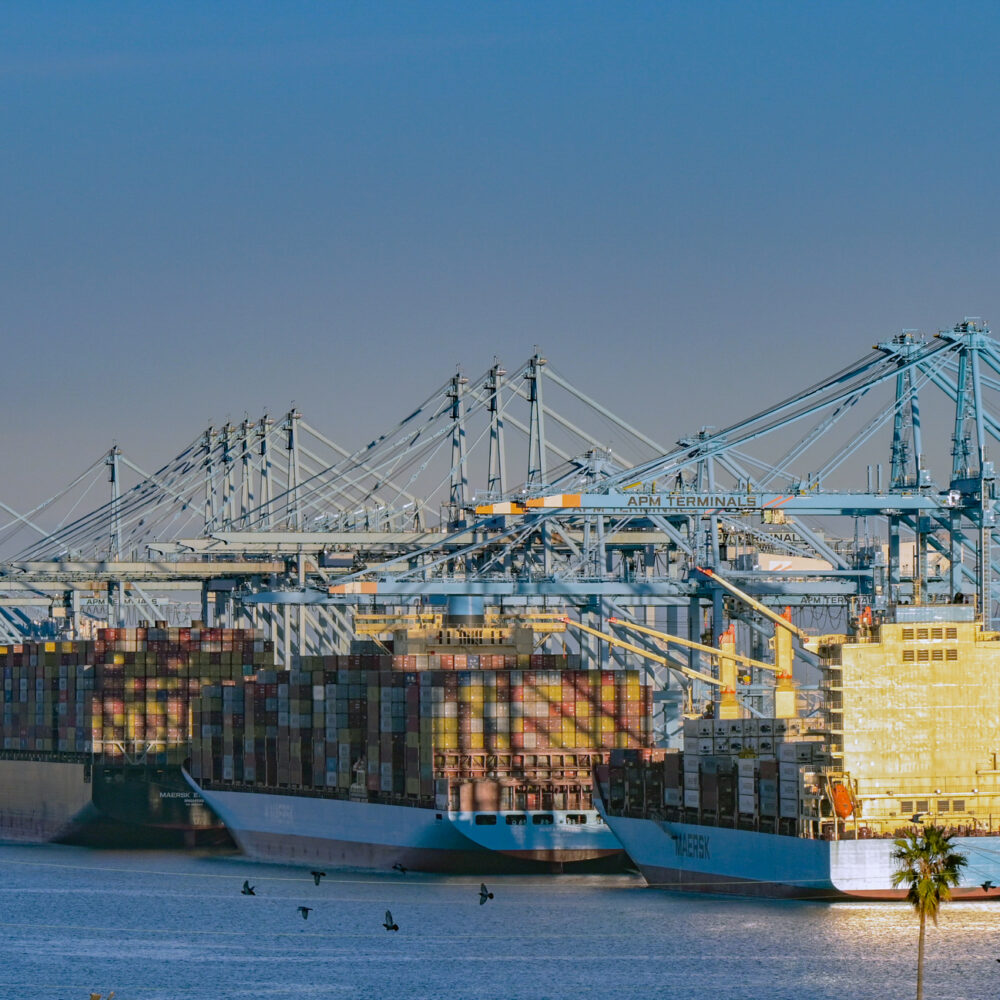 Container ship at port with cranes respresenting USMX and ILA labor negotiations and potential port disruption.
