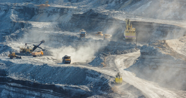 Open-pit mining site with heavy machinery, trucks, and excavators extracting materials in a dusty environment.