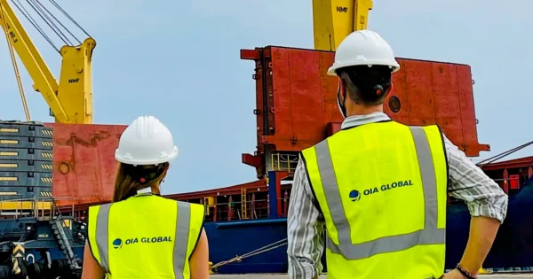 OIA Global employees wearing safety vests and helmets overseeing cargo operations at a port terminal.