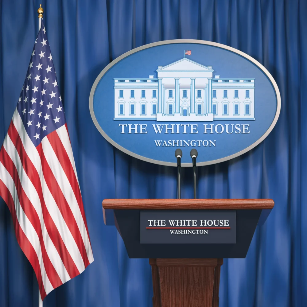 Podium at The White House press briefing room with official signage and U.S. flag against a blue curtain backdrop.