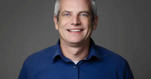 Retrato profissional de um membro da equipe OIA Global vestindo uma camisa azul com colarinho
