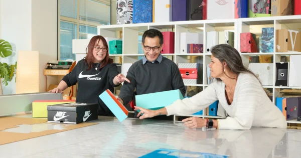 Packaging solutions design studio team collaborating around various box prototypes and materials.