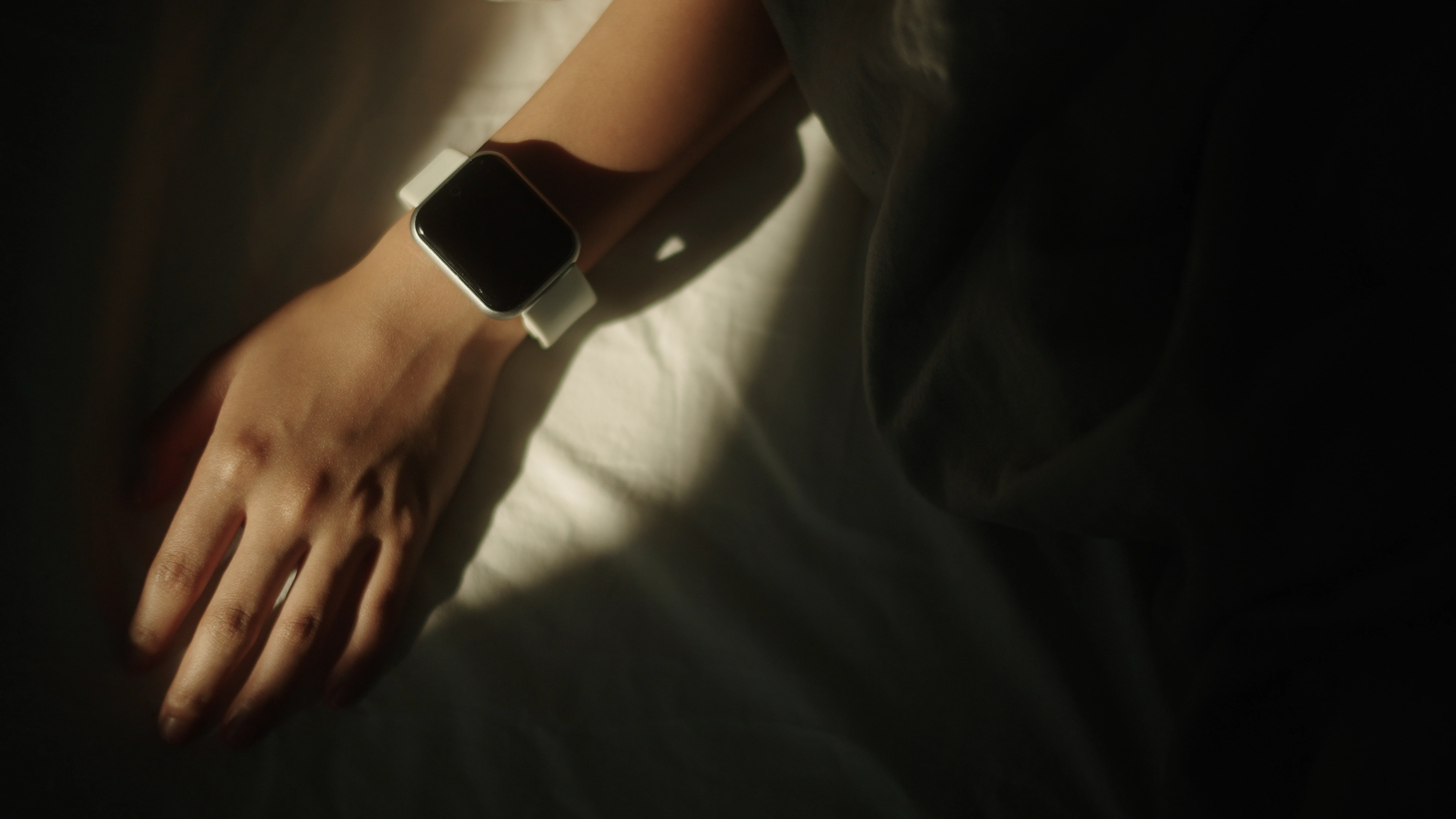 Close-up of a smartwatch on a wrist displaying a dark screen in soft lighting.