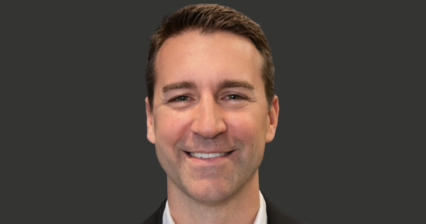Professional corporate headshot of a business professional in a dark suit against a neutral background.