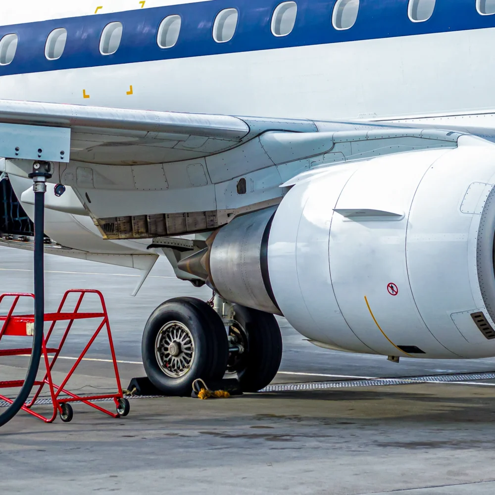 Aircraft engine and wing on airport tarmac with refueling hose connected, illustrating air cargo fueling operations.